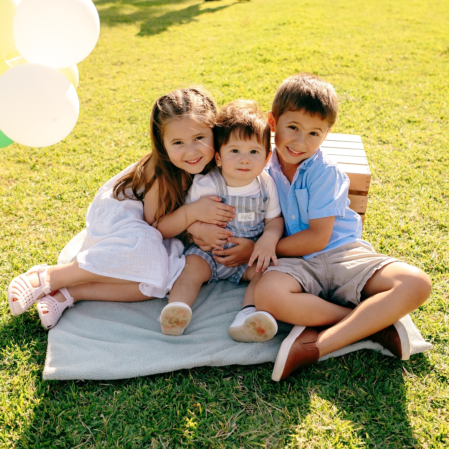 Three children sitting on a blanket outdoors.