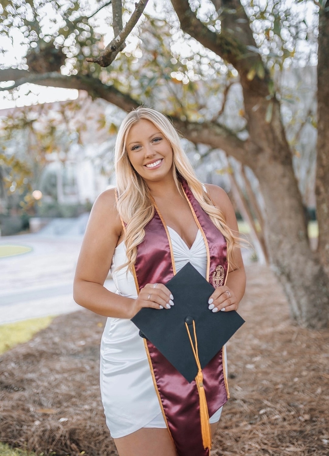 Graduating woman holding cap and gown outdoors.