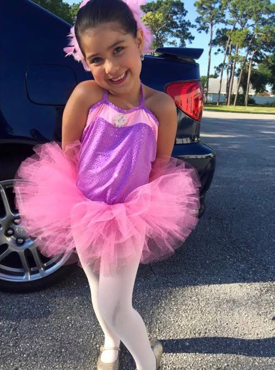 Smiling girl in pink tutu costume outside.